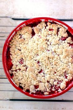 a close up of a pie in a red bowl on a wooden table with utensils