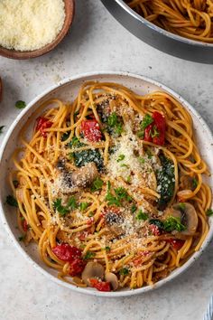 a bowl of pasta with mushrooms, tomatoes and parmesan cheese on the side