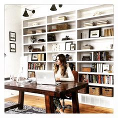 a woman sitting at a desk with a laptop in front of her and bookshelves behind her