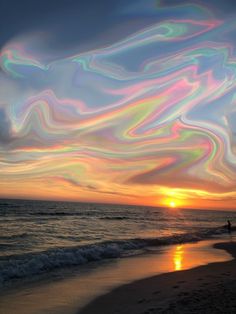 the sun is setting over the ocean with colorful clouds in the sky and people walking on the beach