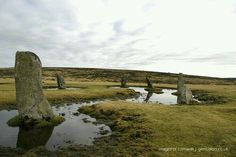 several large rocks sitting in the middle of a grassy field next to a puddle of water