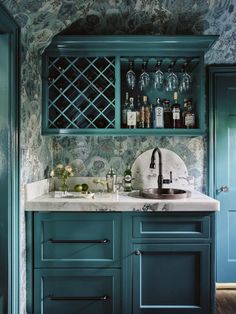 a kitchen with green cabinets and marble counter tops, wine glasses on the shelves above the sink