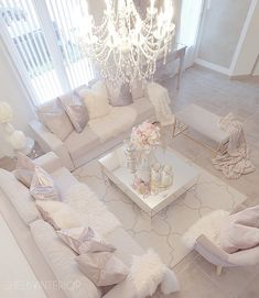 a living room filled with white furniture and a chandelier hanging from the ceiling