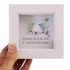 a person holding up a small white frame with two birds on it and the words,'birthday isn't a big thing it's a million little things