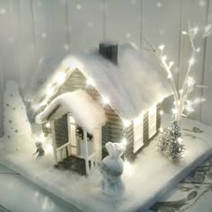 a small christmas house with lights on it's roof and snow falling off the roof