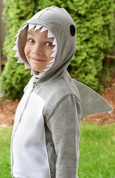 a young boy wearing a shark costume in front of some grass and bushes with his mouth open