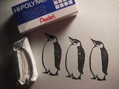 a stamp with three penguins on it next to a piece of paper and a wax block