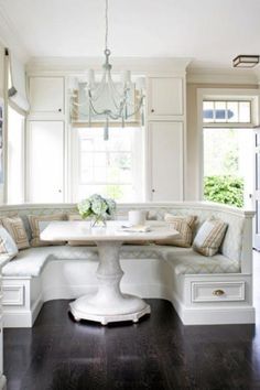 a kitchen with white cabinets and a table in the center, surrounded by built - in seating