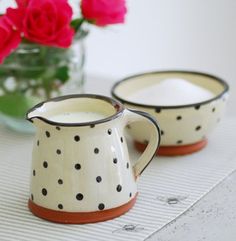 two white and black polka dot mugs with red roses in the background