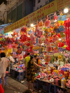 people are shopping at an outdoor market with lots of lanterns and decorations on the wall