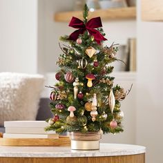 a small christmas tree with ornaments on it and a red bow around the top is sitting on a table