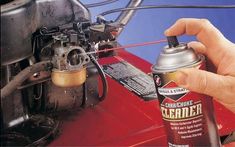 a person is holding a can of spray paint in front of an old car's engine