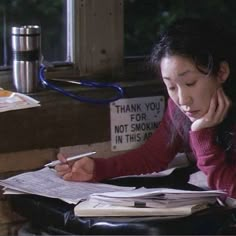 a woman sitting at a table with papers and pens in her hand, writing on a piece of paper