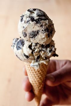 an ice cream cone filled with chocolate chip cookies and oreo chunks, on top of a wooden table