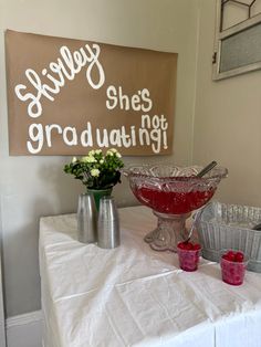 a table topped with bowls and vases filled with flowers next to a sign that says she's graduating