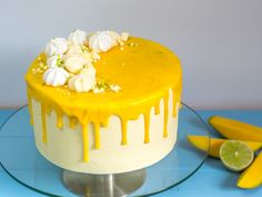 a cake with white and yellow icing sitting on a glass plate next to sliced mangoes