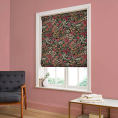 a living room with pink walls and floral patterned roman shades on the window sill