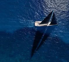 a sailboat floating in the ocean with its shadow on the water's surface