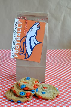 some cookies are sitting on a table next to a brown paper bag with an orange and blue sticker