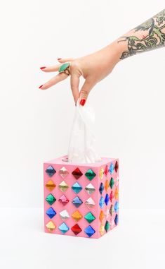 a woman's hand holding a pink bag with multicolored diamonds on it