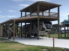 an rv parked in front of a wooden structure with stairs to the second floor and balcony above it