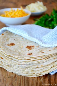 a stack of tortillas sitting on top of a wooden table next to bowls of cheese