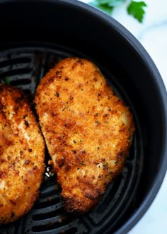 two pieces of chicken cooking in an air fryer with parsley on the side