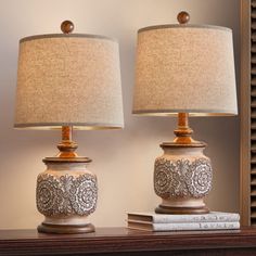 two lamps sitting on top of a wooden table next to a book and lamp shade