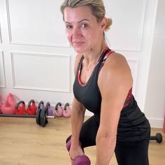 a woman is doing exercises with dumbbells in her home gym, while looking at the camera