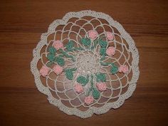 a crocheted doily with pink flowers and green leaves on a wooden surface