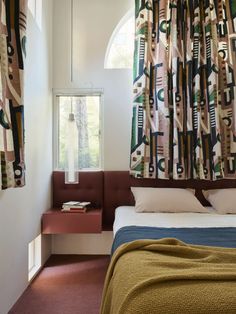 a bed sitting under a window in a bedroom next to a window sill with curtains