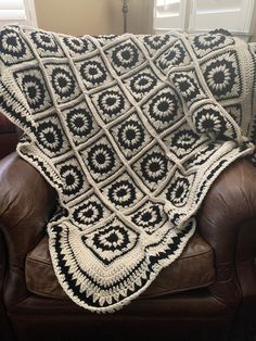 a crocheted blanket is sitting on a brown leather couch in front of a window