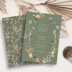 two green wedding cards with floral designs on them next to a silver cup and fan