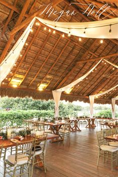 tables and chairs are set up under a thatched roof with lights strung from the rafters