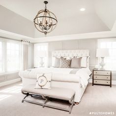 a large white bed sitting under a chandelier in a bedroom next to two windows