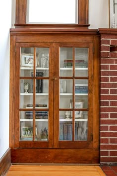 a wooden cabinet with glass doors next to a brick wall