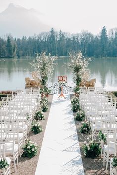 an outdoor ceremony setup with white chairs and flowers on the aisle, overlooking a lake