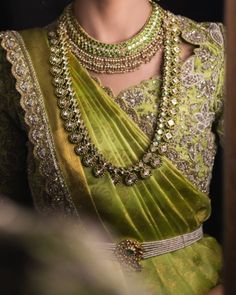 a woman in a green sari with gold jewelry on her neck and chest,