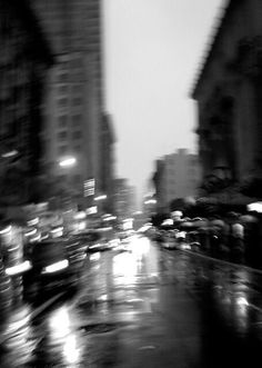 black and white photo of city street at night with cars driving down the wet road