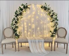 a wedding setup with white flowers and greenery on the headboard, chairs and table