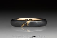 a black and gold wedding band with an arrow on the side, in front of a dark background