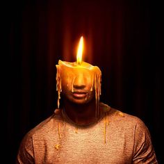 a man with a candle on his head in front of a dark background that has dripping yellow icing