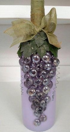 a purple vase with grapes and green leaves on it's top is adorned with a bow