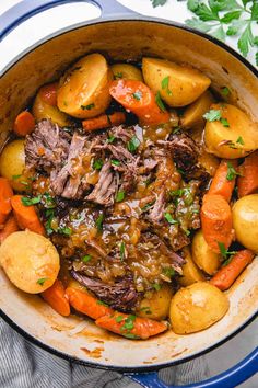 pot roast with carrots, potatoes and parsley in a blue pan on a white table