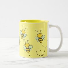 a yellow and white coffee mug with bees painted on the side, sitting on a marble surface