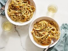 two bowls filled with pasta and garnished with parsley next to a glass of wine