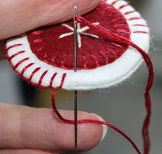 someone is holding a needle and thread in front of a red piece of fabric that has been stitched together