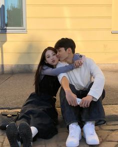 a man and woman sitting on the ground next to each other with their arms around each other