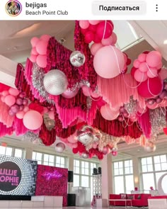 a room filled with lots of pink and silver balloons hanging from the ceiling next to windows