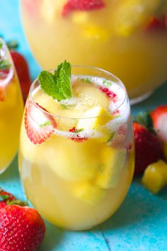 two glasses filled with lemonade and strawberries next to each other on a blue surface